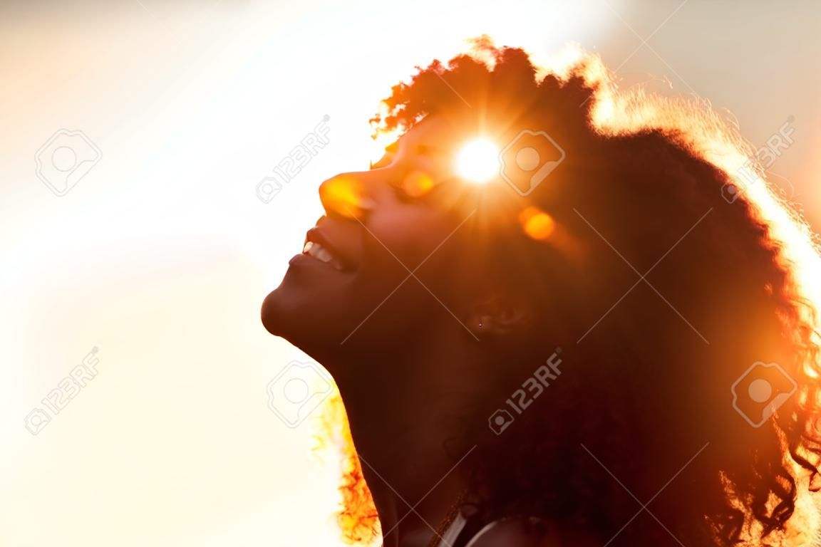 Perfile o perfil de uma mulher bonita com o cabelo do estilo afro mostrado em silhueta contra o alargamento dourado do sol em uma noite do verão