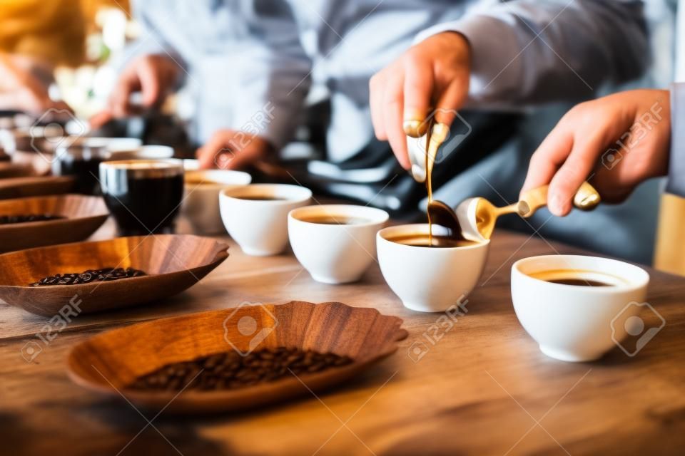Freigestellte Bild der Hände der professionellen Baristas an einem Holztisch mit vielen Tassen, Training, um die perfekte Tasse Kaffee mit einer Vielzahl von gerösteten Kaffeebohnen zu machen