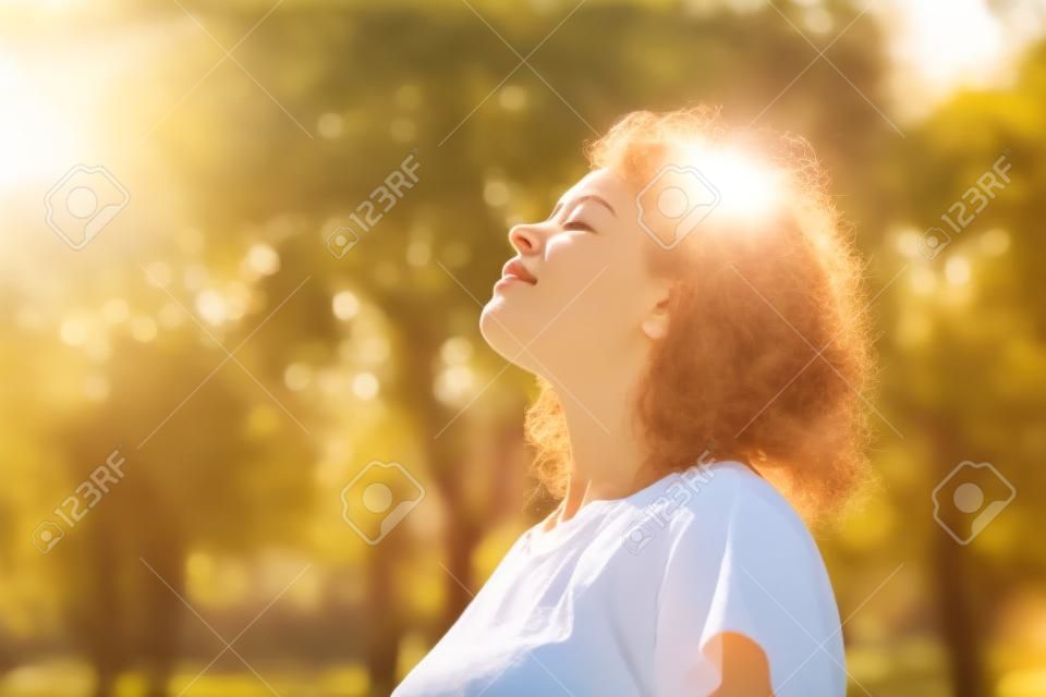 jonge vrouw staan buiten voelen de zon op haar gezicht