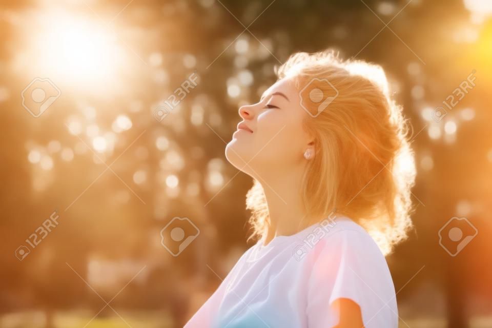 Jeune femme debout à l'extérieur sentant le soleil sur son visage
