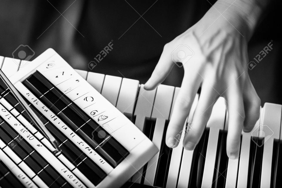 PUBLIC DOMAIN MUSIC SCORE. Close up detail on the hand of a musician composer playing the black and white keys of an electronic  music keyboard and writing notes on the musical stave.