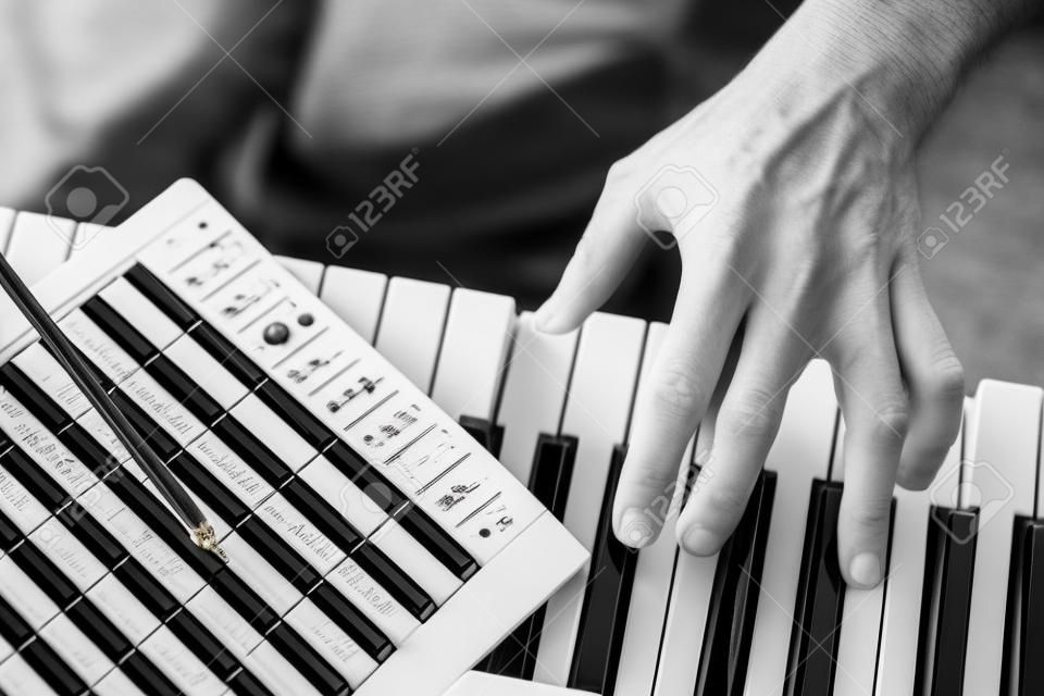 PUBLIC DOMAIN MUSIC SCORE. Close up detail on the hand of a musician composer playing the black and white keys of an electronic  music keyboard and writing notes on the musical stave.