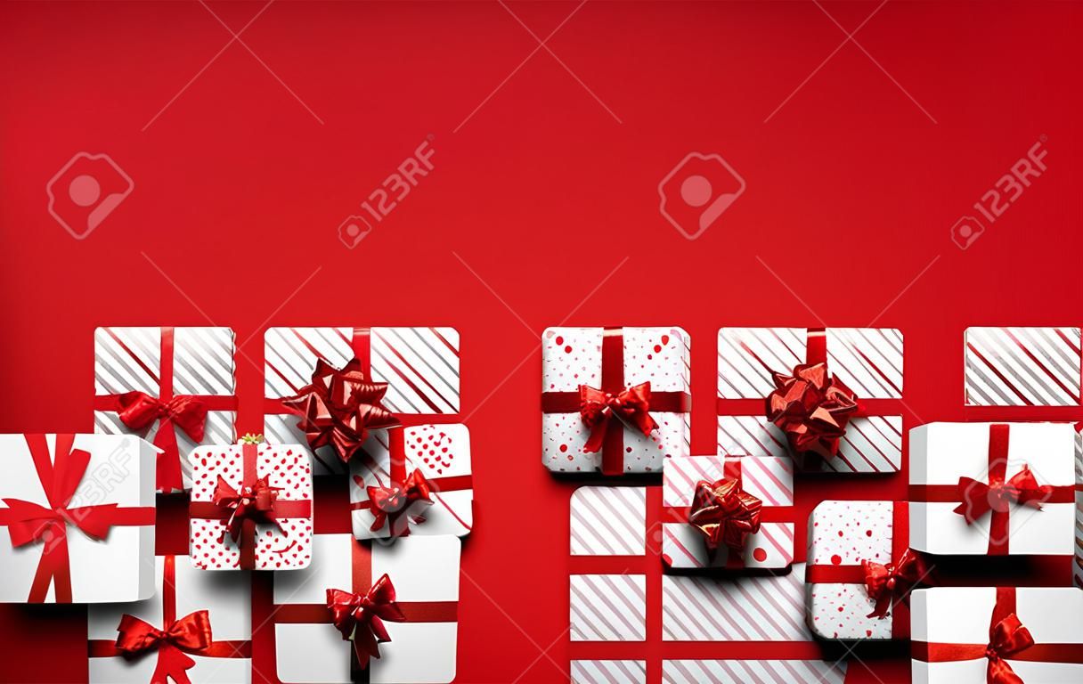 White gift boxes with red bows like triangle Christmas tree form. Red background. Space for text. Vector holiday illustration.