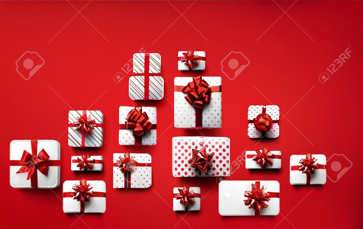 Witte geschenkdozen met rode strikjes zoals driehoekige kerstboom vorm. Rode achtergrond. Ruimte voor tekst. Vector vakantie illustratie.