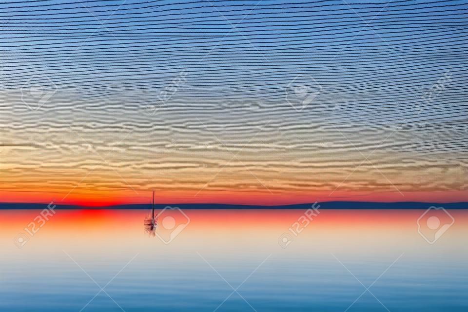 Minimalist view of fishing net poles on a lake, with perfectly still water and empty sky at dusk