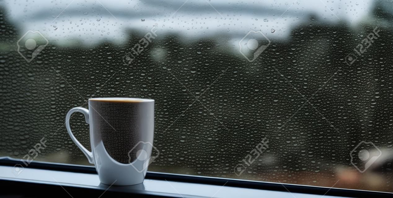 Filiżanka kawy na parapecie z kroplami deszczu na szkle
