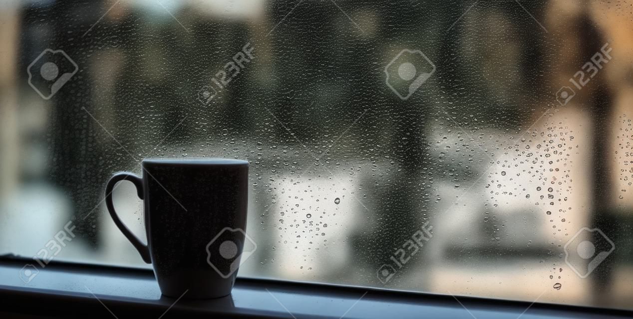 Filiżanka kawy na parapecie z kroplami deszczu na szkle