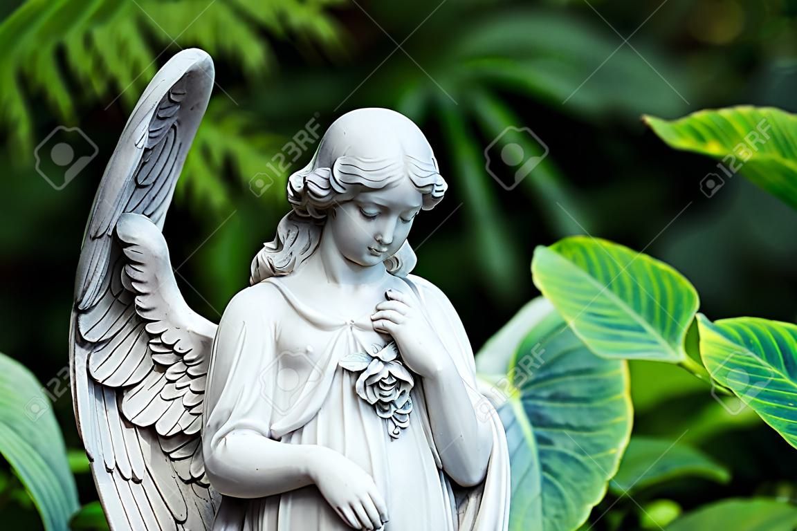 Marble statue of angel with closed eyes at green summer garden background.