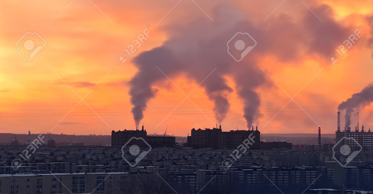 Distrito de la ciudad en la puesta de sol en invierno. Planta industrial en el fondo