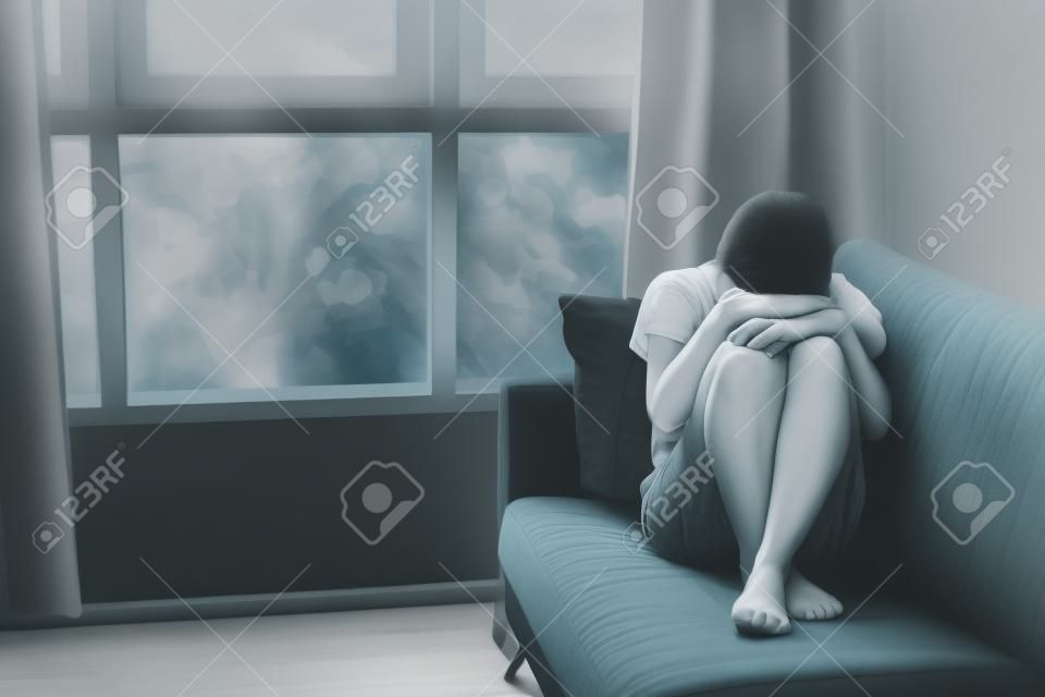 Concetto di depressione e ansia della donna in posizione fetale sul divano con colori cupi. Copia spazio.