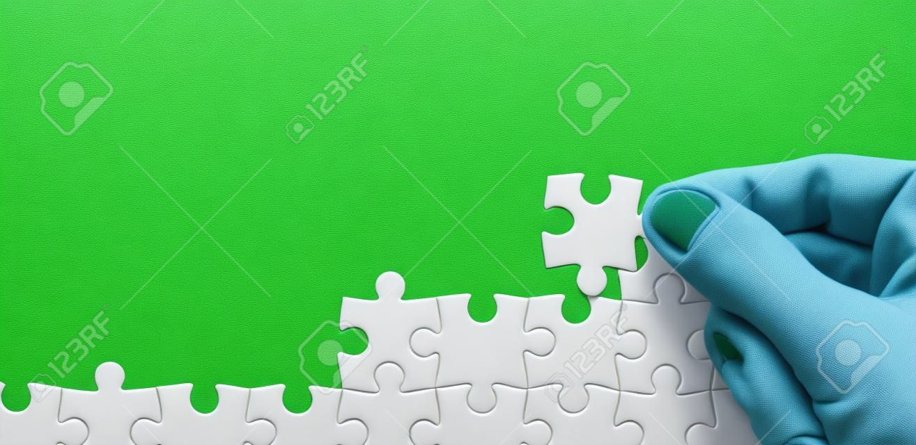 The hand folds a white jigsaw puzzle against the background of the green surface. Texture photo with space for text