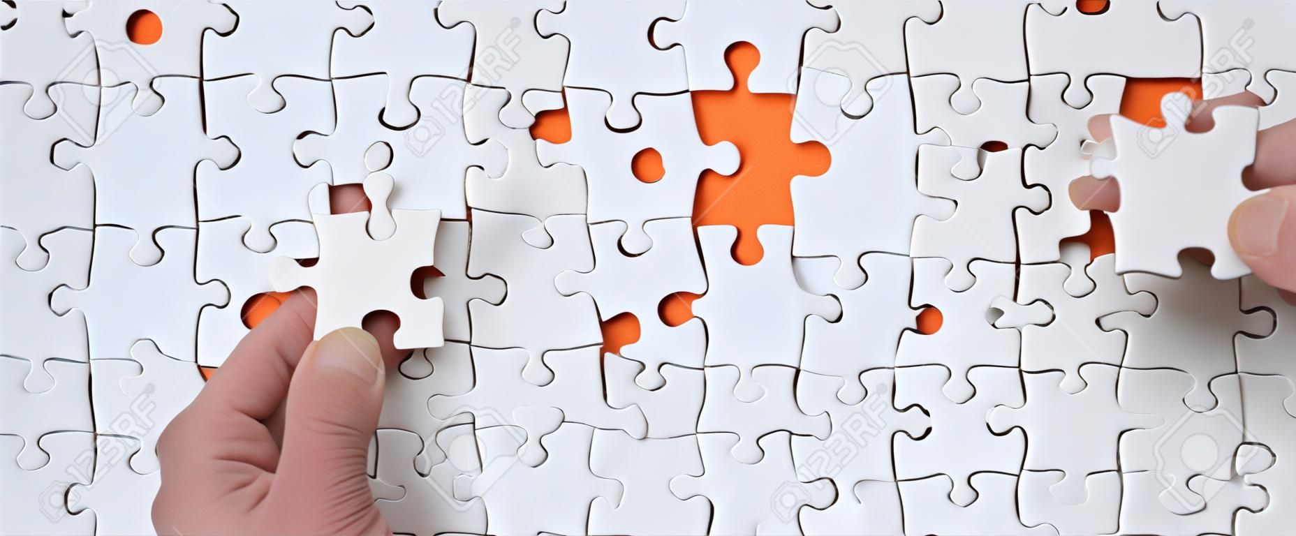The texture of a white jigsaw puzzle in the assembled state with one missing element that the male hand puts in
