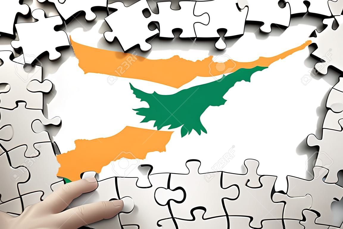 Cyprus flag  is depicted on a table on which the human hand folds a puzzle of white color.