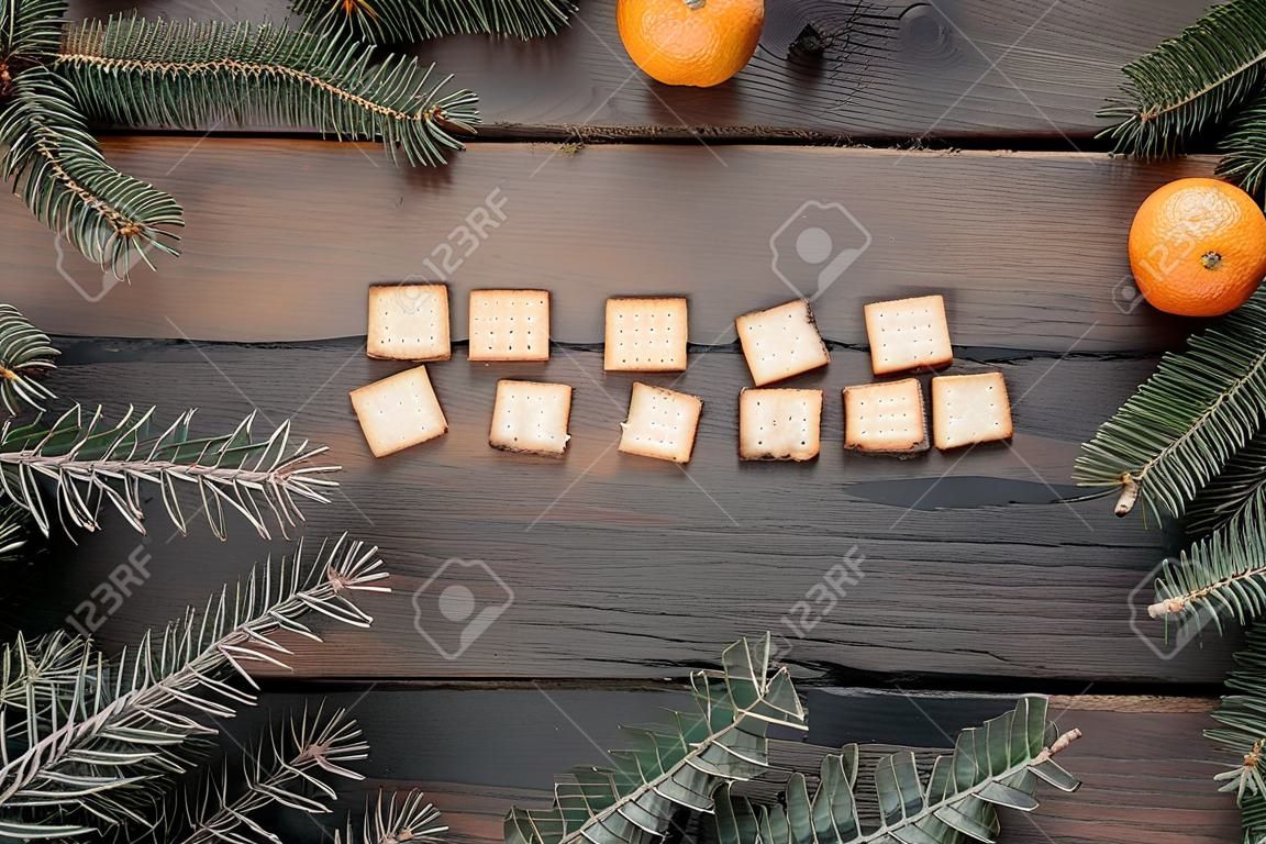Weihnachtsfeiertagskarte mit Mandarinen, Crackertext und Tannenzweigen mit Kopienraum. Ansicht von oben, flach liegend