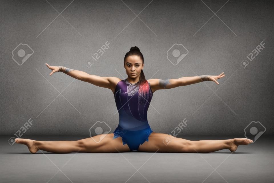 Портрет гимнастка растяжения шпагат на сером фоне