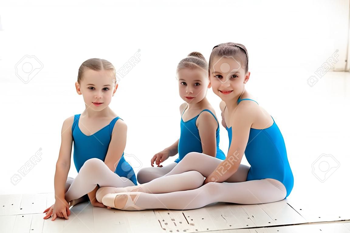 발레 스튜디오에서 흰색 배경에 함께 파란색 수영복과 쁘 신발에 앉아 세 작은 발레 소녀