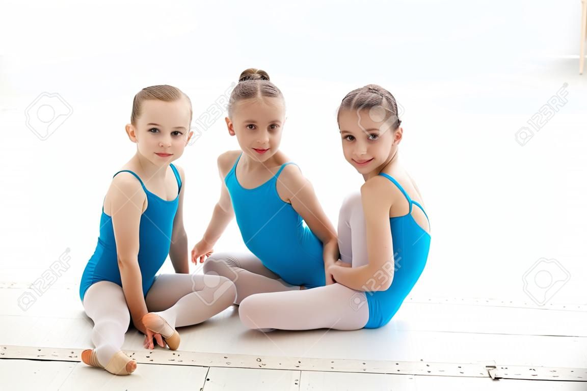 발레 스튜디오에서 흰색 배경에 함께 파란색 수영복과 쁘 신발에 앉아 세 작은 발레 소녀