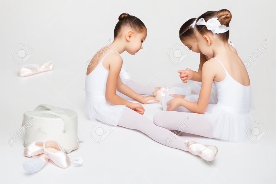 Trois petites filles de ballet assis dans maillot de bain et Pointe chaussures blanches avec chat sur fond blanc dans le studio de ballet