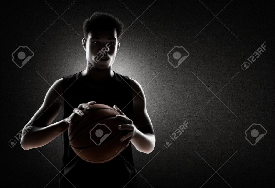 La vista de la silueta de una pelota de baloncesto celebración jugador de baloncesto en el fondo negro