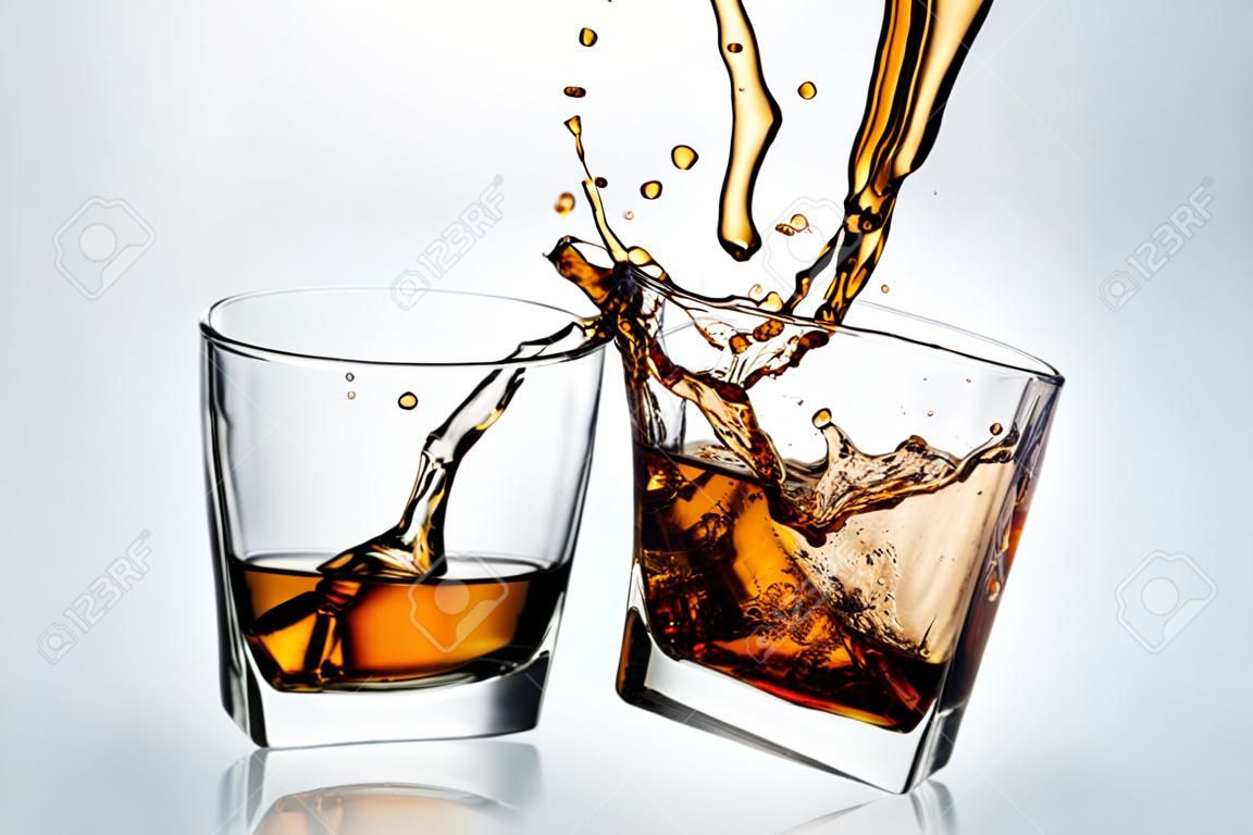 Two whiskey glasses clinking together on gray