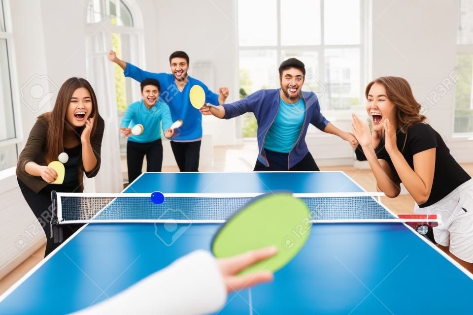 Группа счастливых молодых друзей, играющих в настольный теннис в пинг-понг