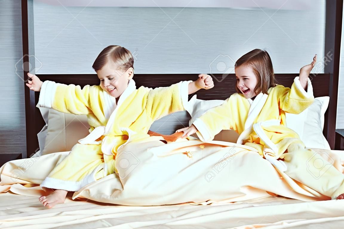 Bambini, ragazzi e ragazze che ridono felici in morbido accappatoio dopo il bagno giocano sul letto bianco