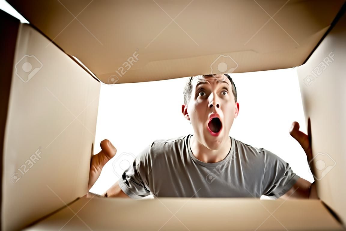 El hombre sorprendido desempacando, abriendo la caja de cartón y mirando dentro. El concepto de estilo de vida de paquete, entrega, sorpresa, regalo. Conceptos de emociones y expresiones faciales humanas