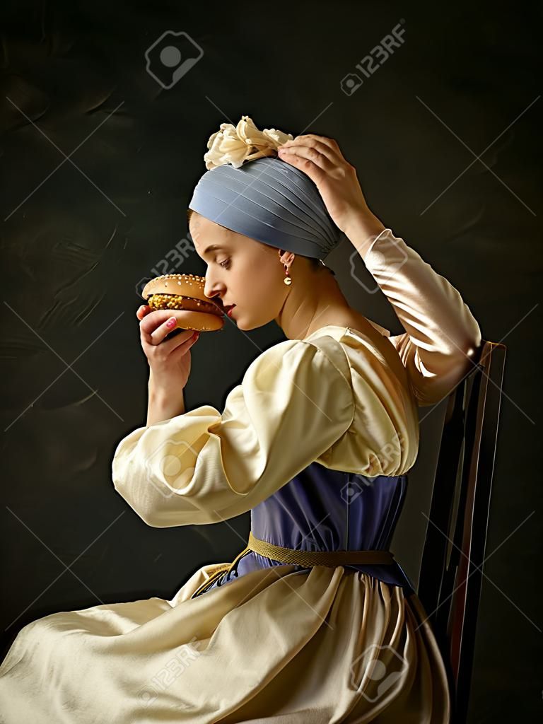 Medieval Woman in Historical Costume Wearing Corset Dress and Bonnet with burger. Beautiful peasant girl wearing thrush costume