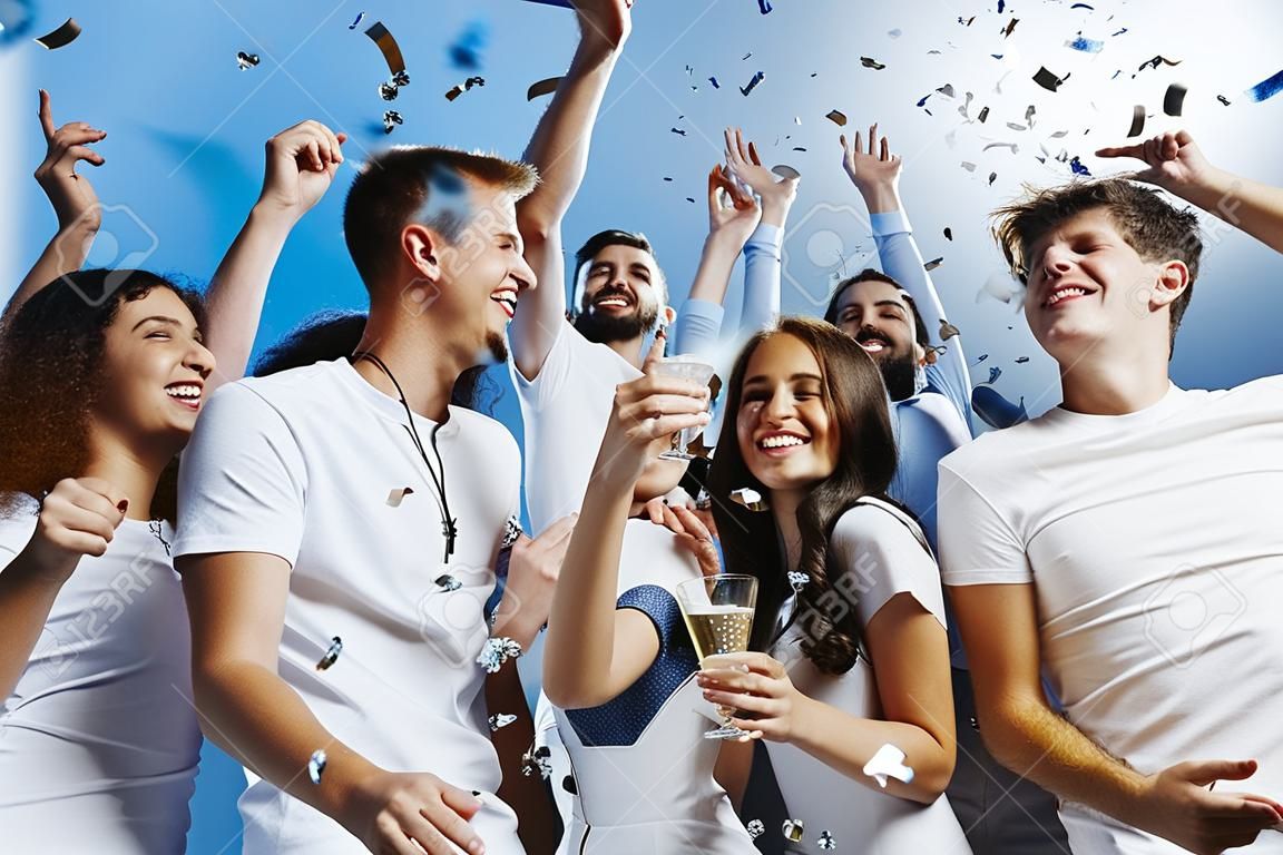 Gruppe fröhlicher, fröhlicher junger Menschen, die zusammen vor blauem Studiohintergrund stehen und feiern
