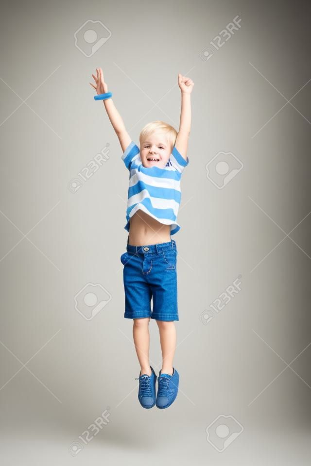 Adorable niño rubio saltando y levanta las manos. Aislado sobre fondo blanco. Disparos en el estudio