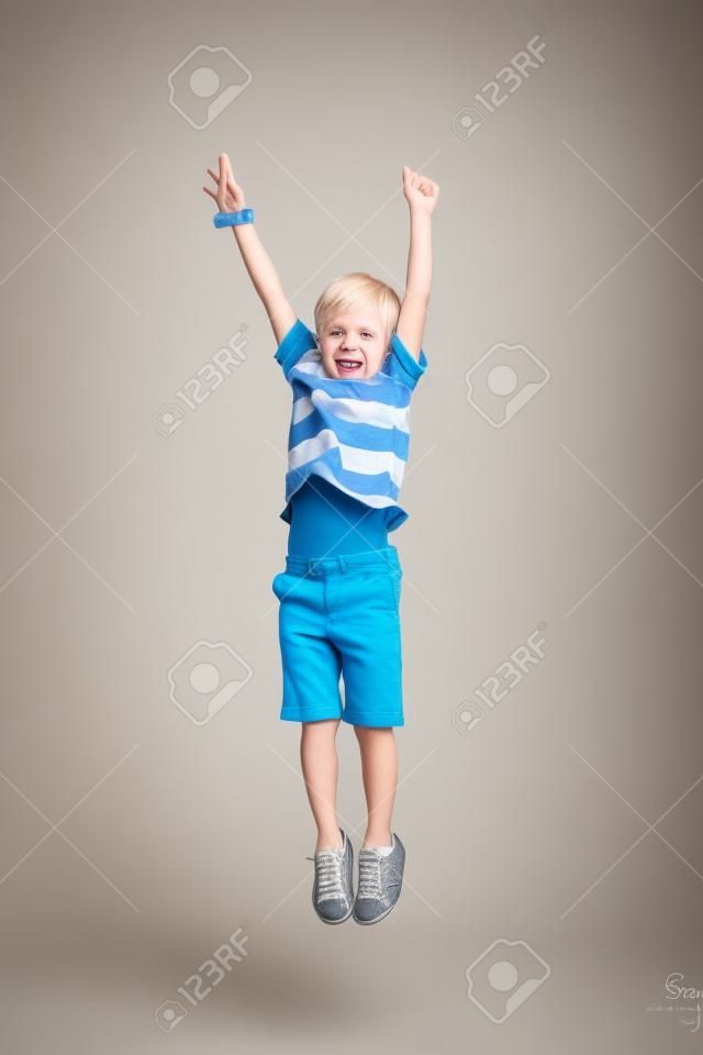 Entzückender blonder Junge springt und hebt seine Hände hoch. Isoliert auf weißem Hintergrund. Shooting im Studio