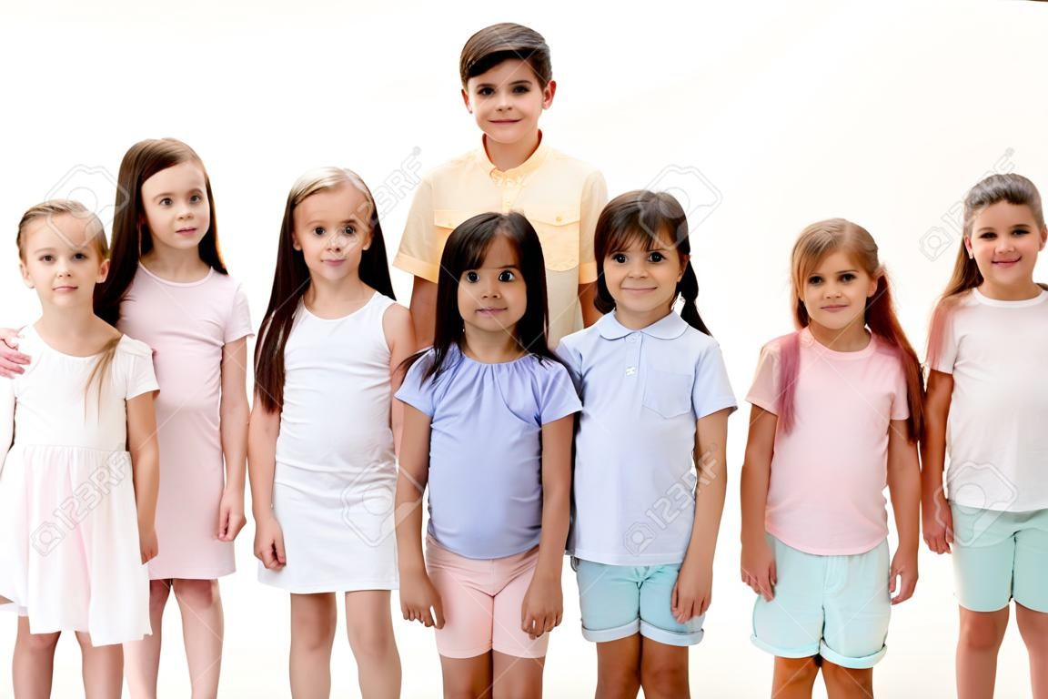 Das Porträt von glücklichen, süßen kleinen Kindern, Jungen und Mädchen in stilvoller Freizeitkleidung, die die Kamera gegen die weiße Studiowand betrachten. Konzept für Kindermode und menschliche Emotionen