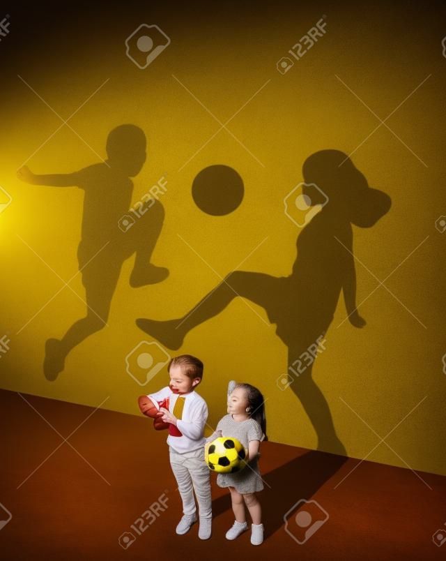 규칙이 없는 진정한 플레이. 순수한 감정. 어린 시절과 꿈 개념입니다. 노란색 스튜디오 벽에 아이와 그림자가 있는 개념적 이미지. 어린 소년과 소녀는 함께 축구를 하고 싶어합니다.