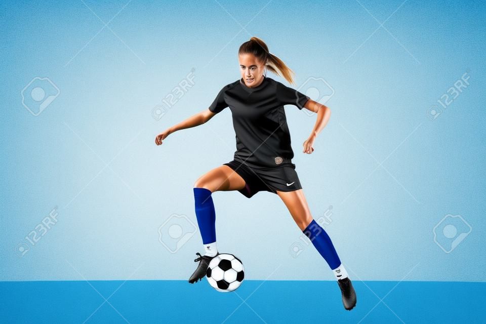 Joven jugadora de fútbol o fútbol con cabello largo en ropa deportiva y botas pateando la pelota para el gol en salto aislado en fondo blanco. Concepto de estilo de vida saludable, deporte profesional, hobby.