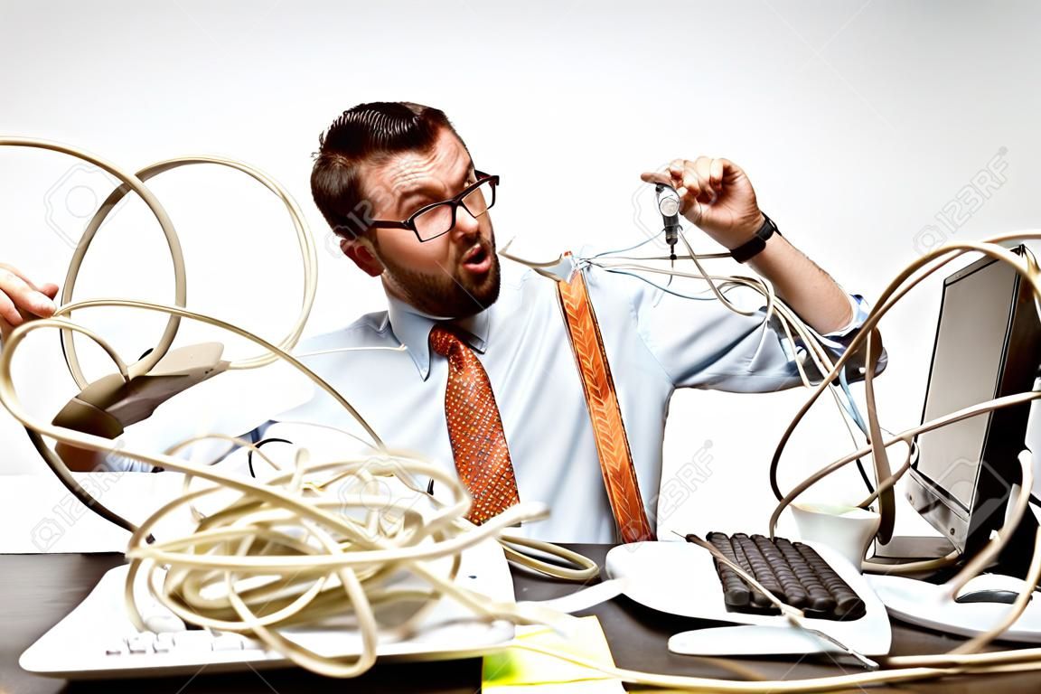 Completely confused. There are a lot of wires in the workplace and man is constantly tangled in them. Its literally blocking him. Concept of office workers troubles, business, problems and stress.