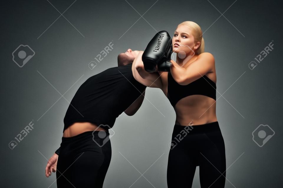 Homme en tenue noire et femme caucasienne athlétique combats sur fond de studio blanc. Autodéfense des femmes, droits, concept d'égalité. Faire face à la violence domestique ou au vol dans la rue.