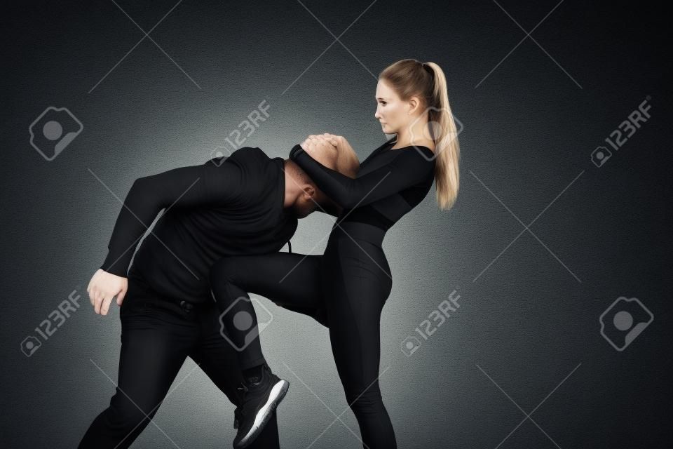 Homem de roupa preta e mulher caucasiana atlética que luta no fundo branco do estúdio. Autodefesa das mulheres, direitos, conceito da igualdade. Enfrentando a violência doméstica ou o roubo na rua.