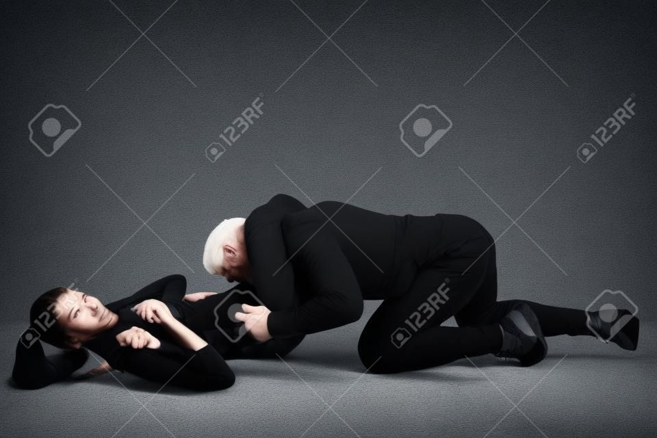 Homme en tenue noire et femme caucasienne athlétique combats sur fond de studio blanc. Autodéfense des femmes, droits, concept d'égalité. Faire face à la violence domestique ou au vol dans la rue.