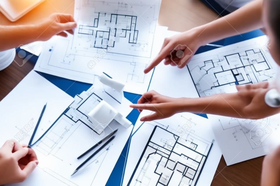건축가-엔지니어의 손의 상위 뷰는 젊은 부부에게 미래의 집, 사무실 또는 상점 디자인 계획을 보여줍니다. 건설 사무실에서 만나 외관, 실내 장식, 집 배치에 대해 이야기합니다.