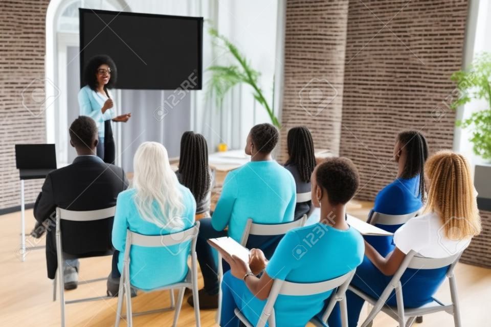 Vrouwelijke Afrikaans-Amerikaanse spreker geven presentatie in hal op de workshop. Publiek of hal. Achteraanzicht van deelnemers aan het publiek. Conferentie evenement, training. Onderwijs, diversiteit, inclusief concept.
