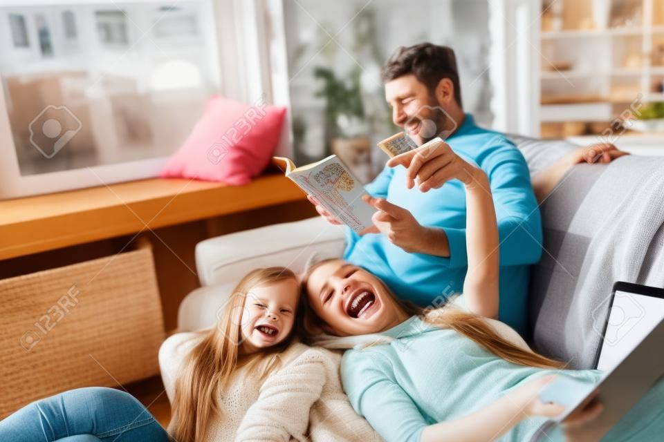 Mãe, pai e filha em casa se divertindo, conforto e conceito acolhedor. Parece feliz, alegre, alegre. Bela família caucasiana. Passar tempo juntos, ler livros, usar dispositivos, tirar selfie.