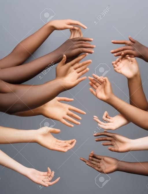 Humanidade. Mãos de pessoas diferentes em contato isoladas em fundo de estúdio cinza. Conceito de relação, diversidade, inclusão, comunidade, união. Toque sem peso, criando uma unidade.