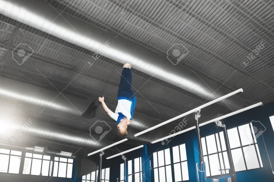 Skillful. Little male gymnast training in gym, composed and active. Caucasian fit boy, athlete in sportswear practicing in exercises for strength, balance. Movement, action, motion, dynamic concept