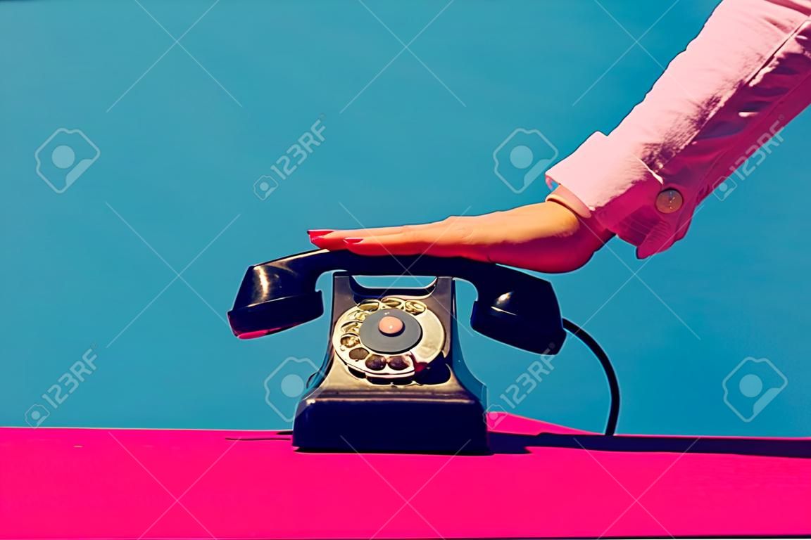 Przedmioty retro, gadżety. żeńska ręka trzyma słuchawkę rocznika telefon odizolowywający na błękitnym i różowym tle. vintage, retro styl mody. fotografia pop-artu.