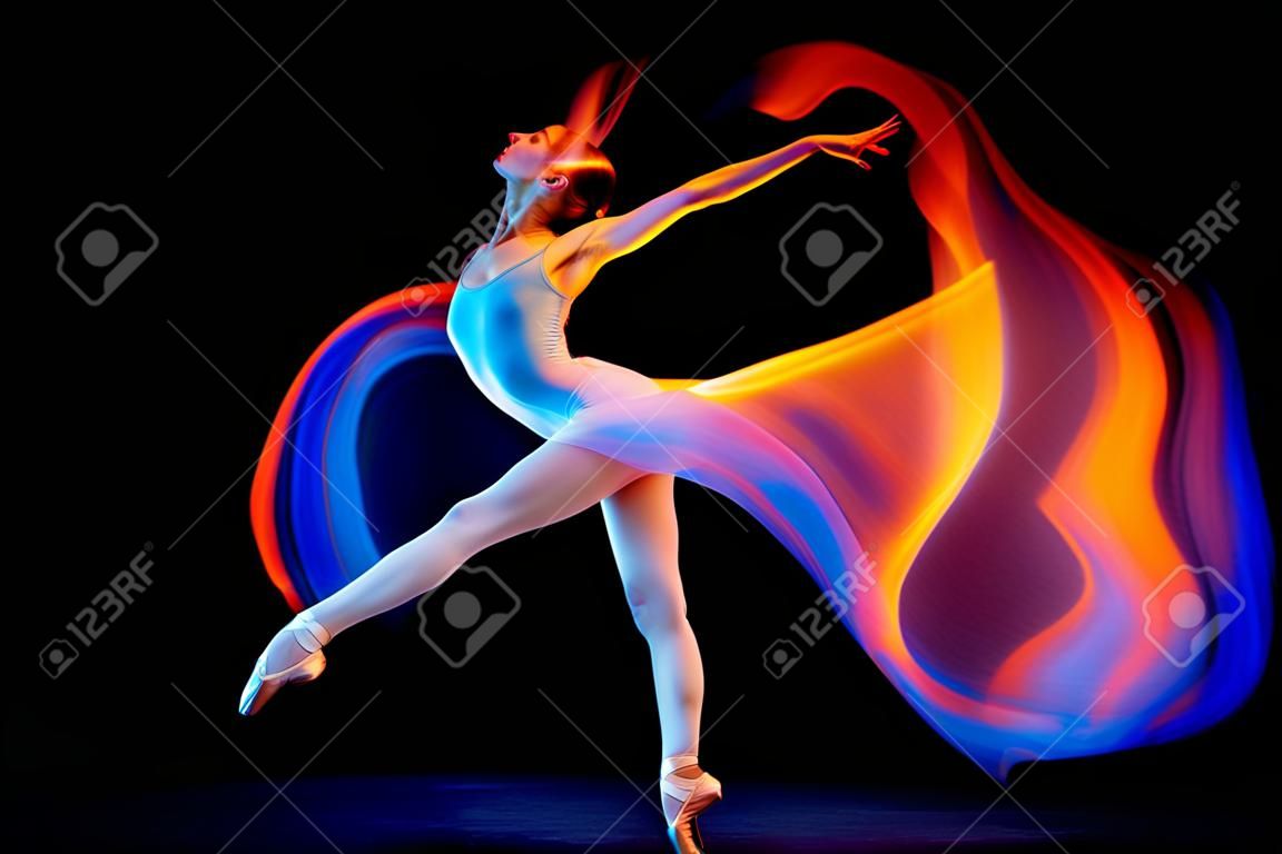 Dynamic portrait of tender slim girl, female ballet dancer in art performance isolated over black background in mixed bright neon light.