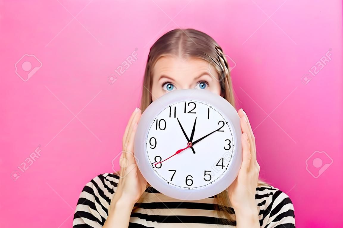 Jeune femme tenant une horloge montrant près de 12