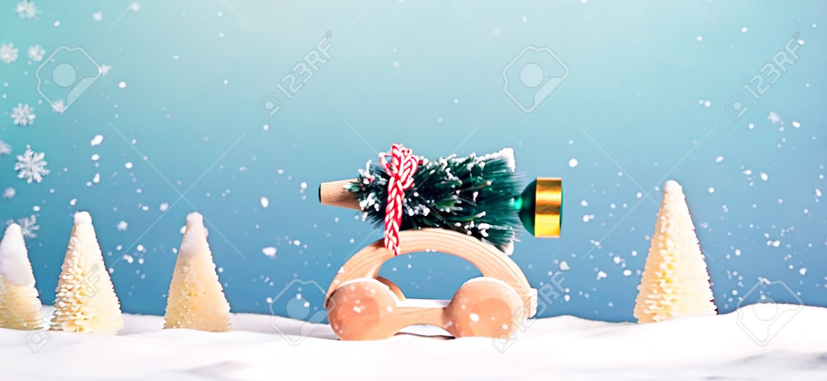 Hölzernes Miniaturauto, das einen Weihnachtsbaum auf einem blauen Hintergrund trägt