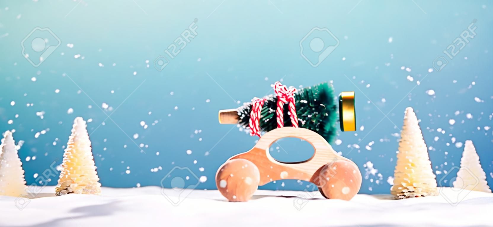 Hölzernes Miniaturauto, das einen Weihnachtsbaum auf einem blauen Hintergrund trägt