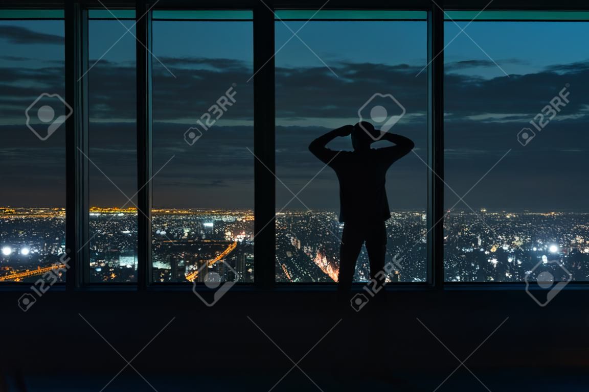 夜に広がる都市の上に大きな窓を見ている男