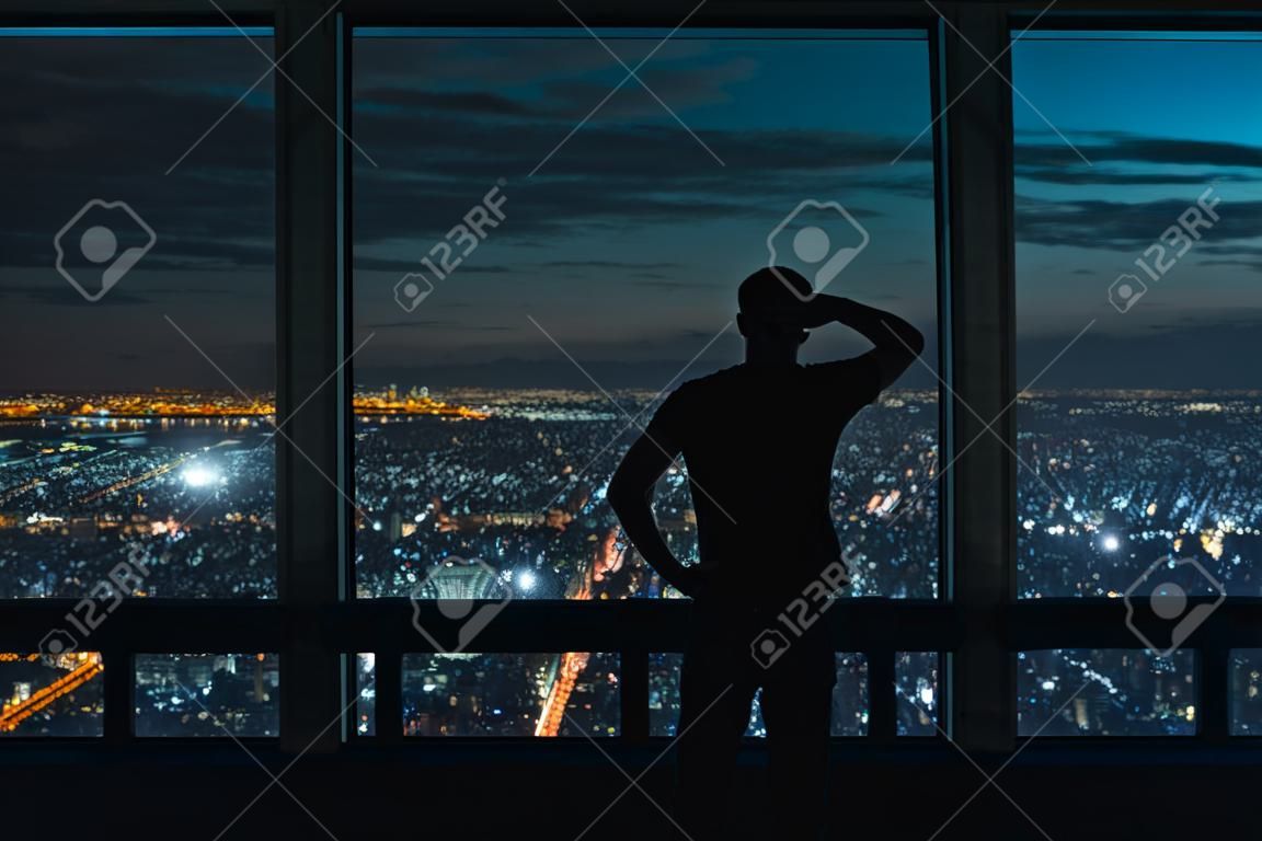 夜に広がる都市の上に大きな窓を見ている男